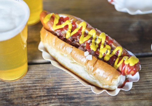 A hot dog with mustard and ketchup and a glass of beer on a wooden table.