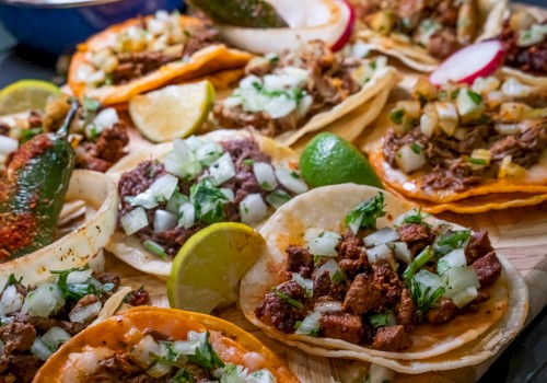 The image shows a variety of delicious-looking tacos with different fillings and lime wedges.